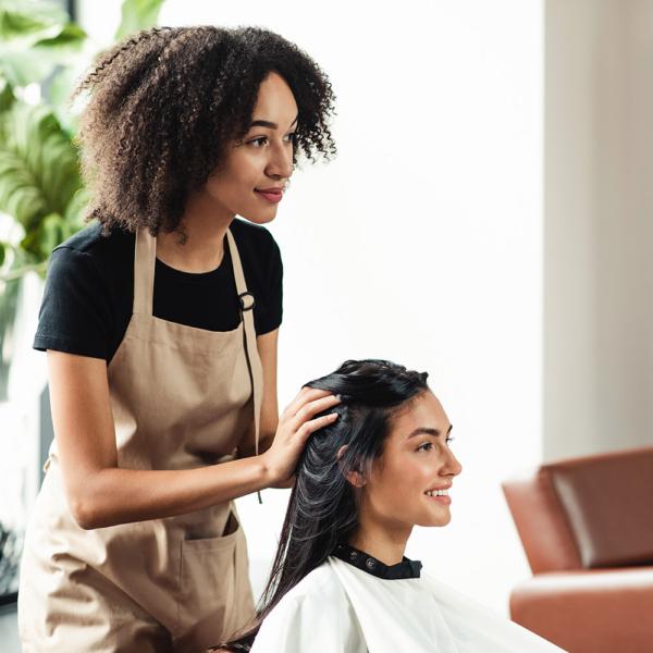 An African American woman is a hairstylist and salon owner talking with a client about their hair